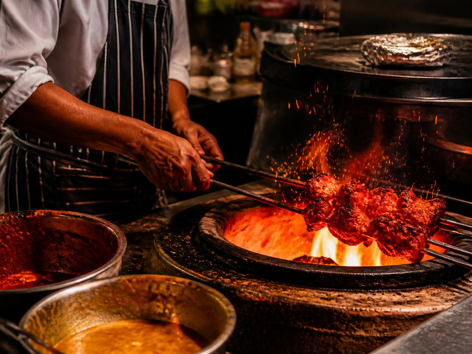 Skewers of tandoori chicken sizzling over an open flame in the tandoor